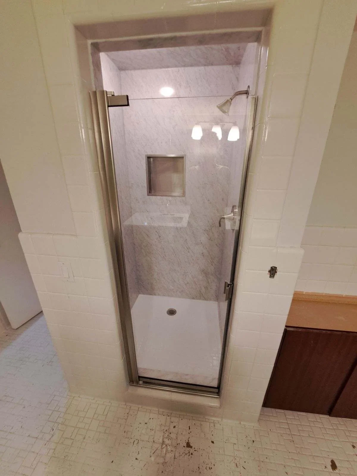 Marble tile shower with frameless glass door, white base pan, and recessed lighting