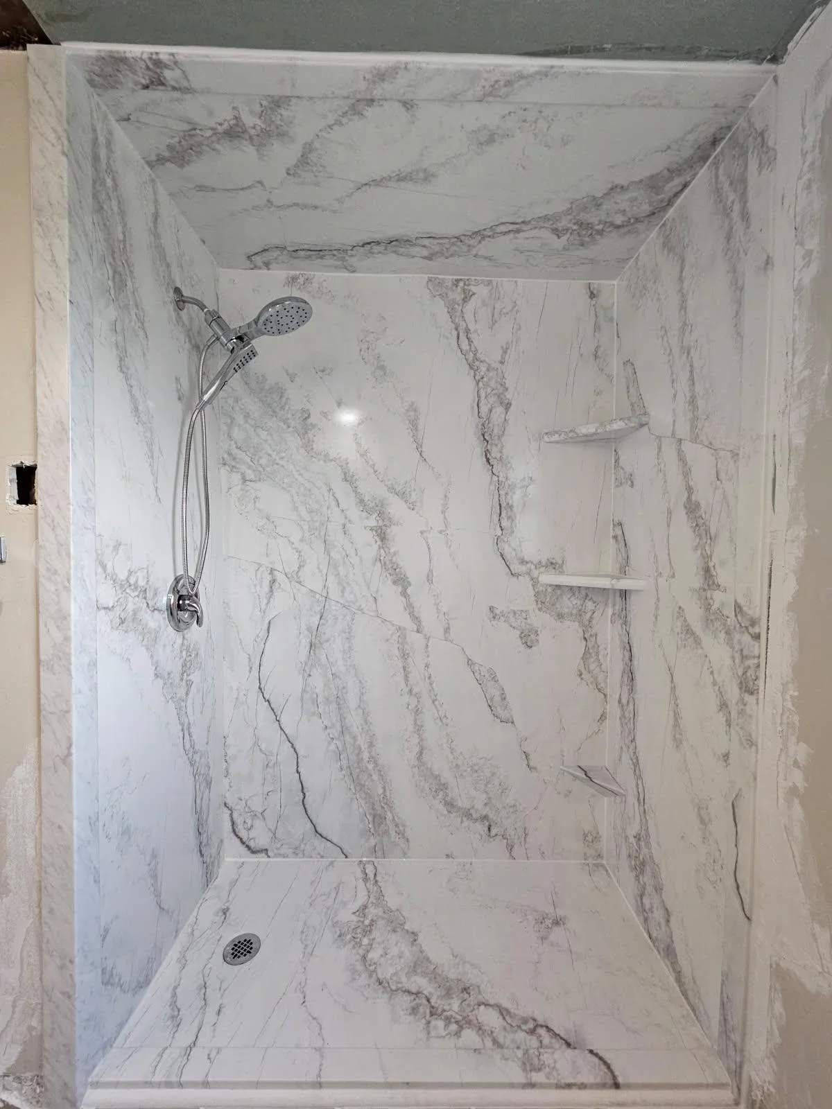 White marble-look tile shower with dual showerhead, chrome fixtures, and matching floor