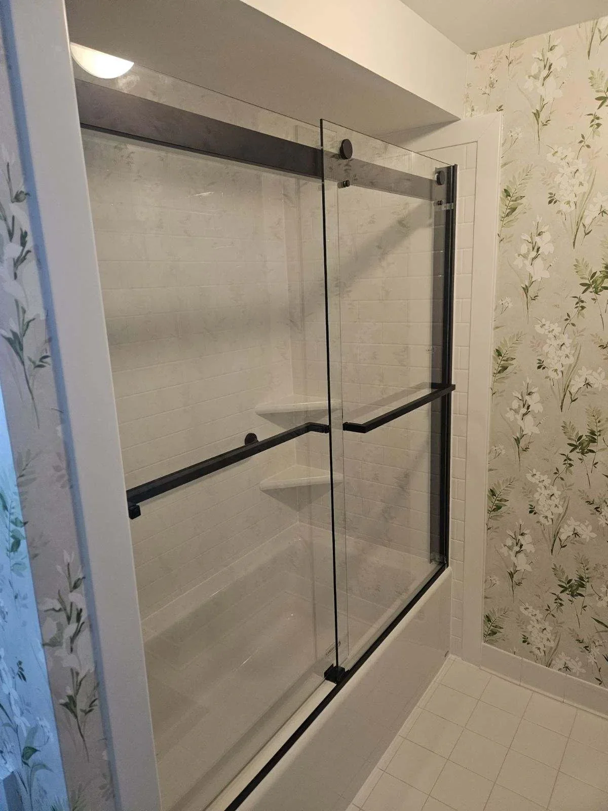 Frameless glass shower enclosure with black hardware and sliding doors in tiled bathroom